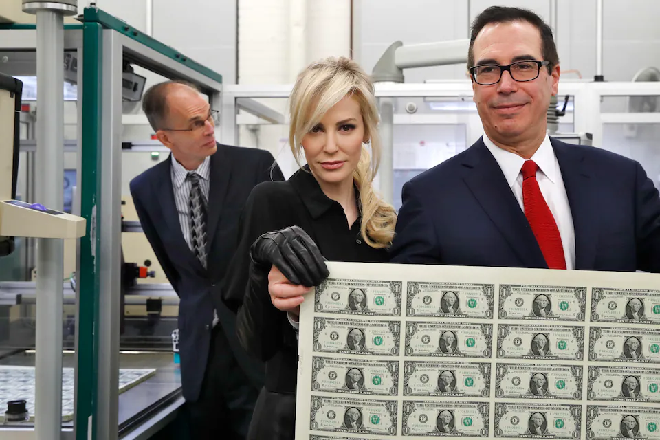 Treasury Secretary Steven Mnuchin, right, and his wife, Louise Linton, hold up a sheet of new $1 bills on Nov. 15 at the Bureau of Engraving and Printing in Washington. (Jacquelyn Martin/AP)